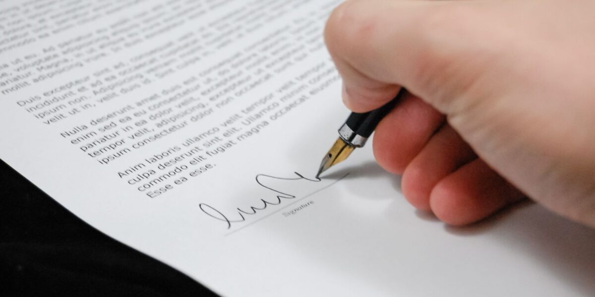 Close-up of a hand signing a property document with a pen, representing land document verification before buying a plot in Chennai